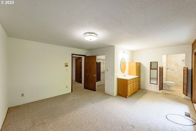 unfurnished bedroom with light colored carpet, a textured ceiling, and ensuite bath