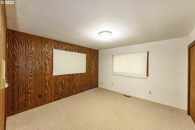 spare room featuring carpet, a textured ceiling, and wood walls