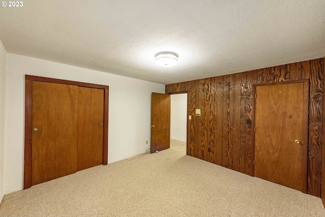 unfurnished bedroom featuring a textured ceiling, carpet floors, a closet, and wood walls