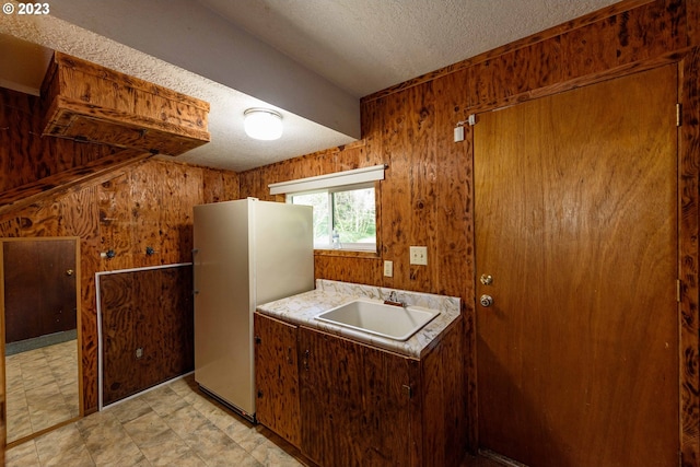 kitchen featuring a textured ceiling, white fridge, sink, and wooden walls