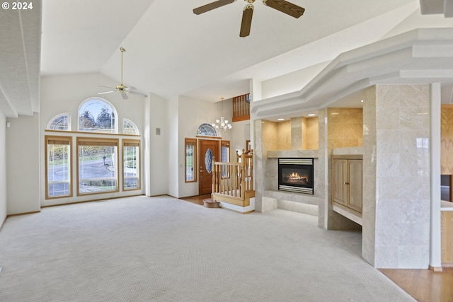 unfurnished living room with a tile fireplace, carpet flooring, ceiling fan with notable chandelier, and high vaulted ceiling