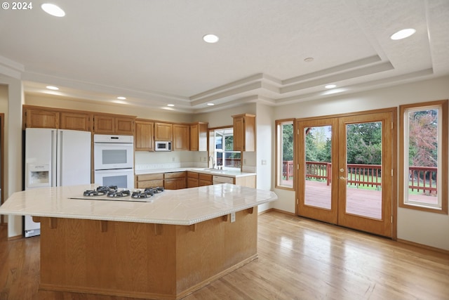 kitchen featuring white appliances, a kitchen bar, a tray ceiling, and light wood-type flooring