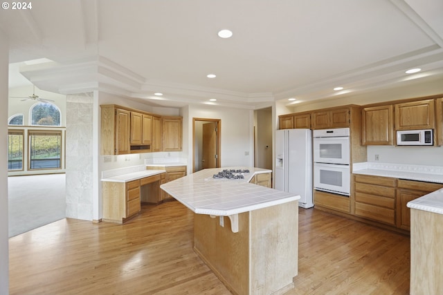 kitchen with white appliances, tile counters, a center island, and light hardwood / wood-style floors