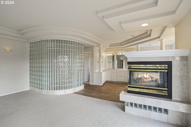 unfurnished living room with carpet floors, a tray ceiling, decorative columns, and a tile fireplace