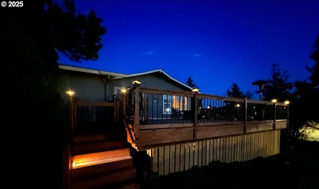 back of house at twilight with a deck, fence, and stucco siding