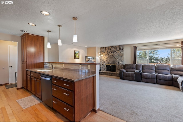 kitchen with a sink, dishwasher, a textured ceiling, a peninsula, and open floor plan