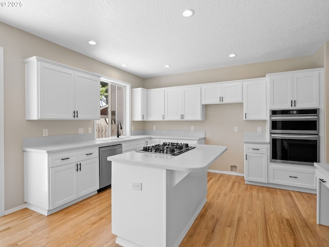 12576 NW Maplecrest Way, Banks, OR 97106 - kitchen featuring appliances with stainless steel finishes, a textured ceiling, light wood-style flooring, white cabinetry, and light countertops