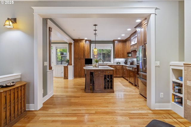 kitchen with brown cabinets, appliances with stainless steel finishes, a kitchen island with sink, and light wood finished floors