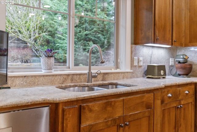 kitchen with decorative backsplash, brown cabinets, light stone countertops, and a sink