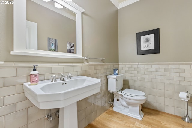 bathroom with wood finished floors, a wainscoted wall, ornamental molding, tile walls, and toilet