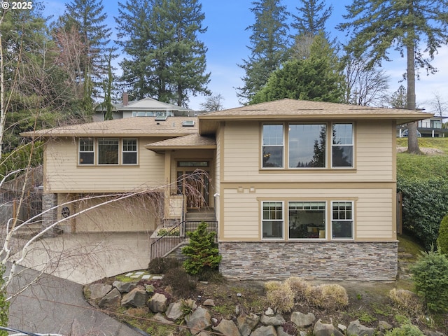 bi-level home featuring a garage, stone siding, and driveway