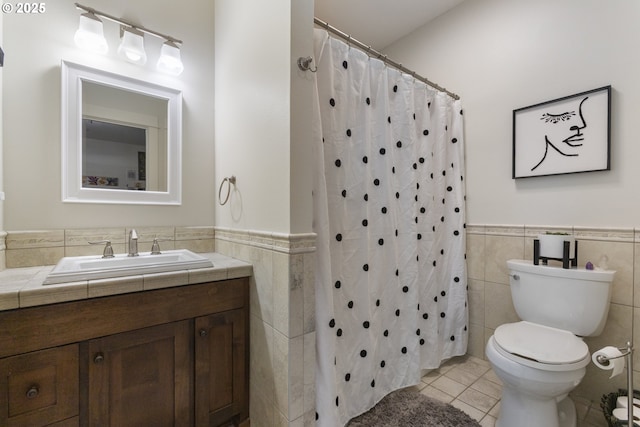 full bath with tile patterned floors, a wainscoted wall, toilet, and tile walls