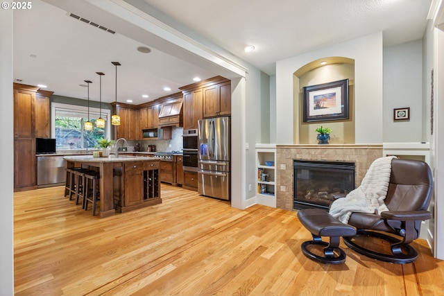 kitchen featuring a breakfast bar, a tiled fireplace, open floor plan, stainless steel appliances, and light wood finished floors