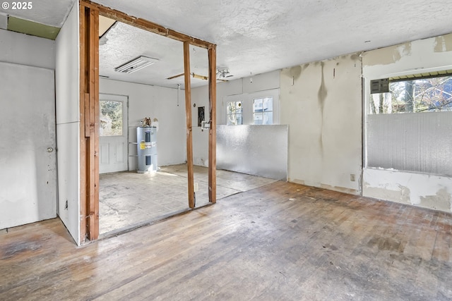 basement featuring water heater, a textured ceiling, wood finished floors, and a wealth of natural light