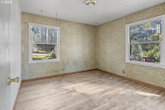 spare room with wallpapered walls, wood finished floors, and baseboards