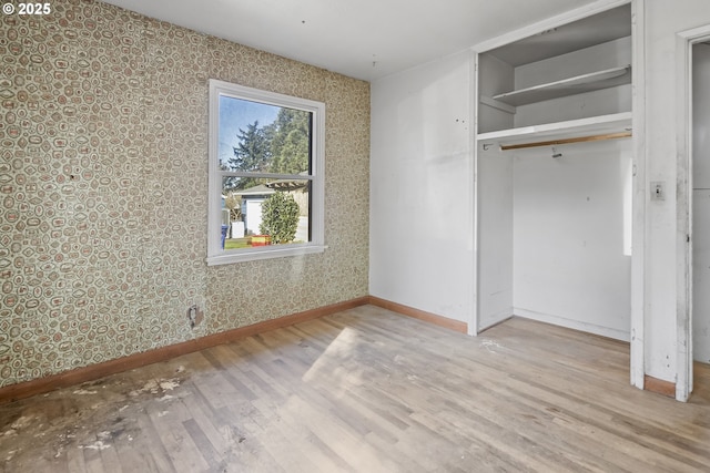 unfurnished bedroom with wallpapered walls, a closet, baseboards, and wood finished floors