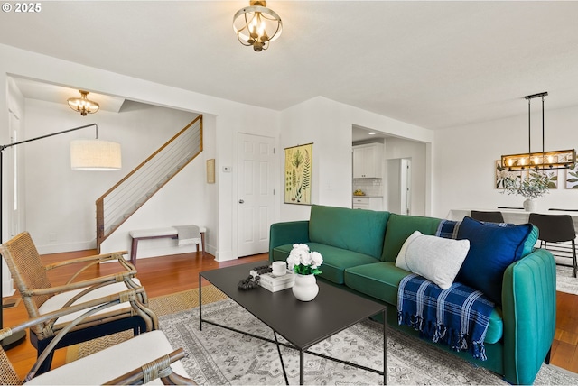 living room with an inviting chandelier, wood finished floors, baseboards, and stairs