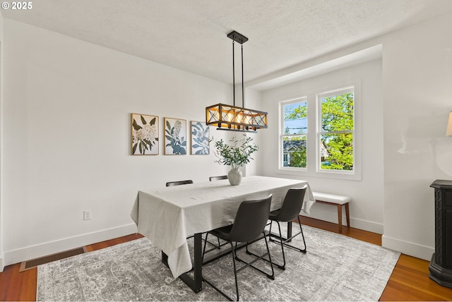 dining room with baseboards, visible vents, a textured ceiling, and wood finished floors