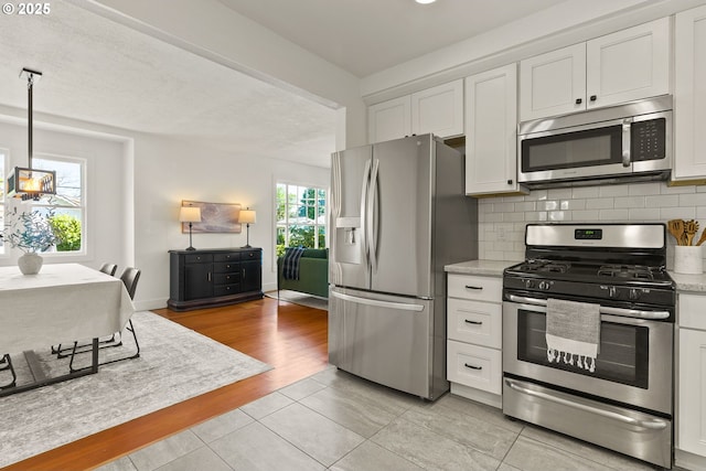 kitchen featuring stainless steel appliances, white cabinetry, baseboards, decorative backsplash, and light tile patterned flooring