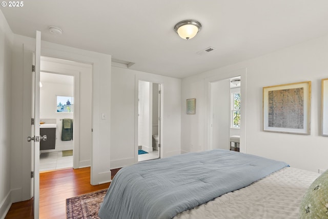 bedroom with baseboards, visible vents, and wood finished floors