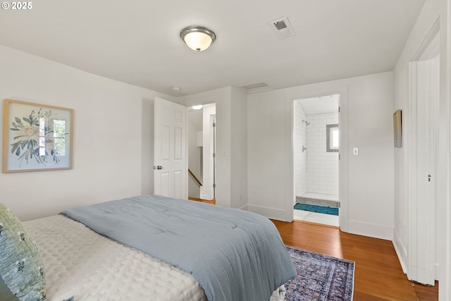 bedroom with connected bathroom, wood finished floors, attic access, visible vents, and baseboards
