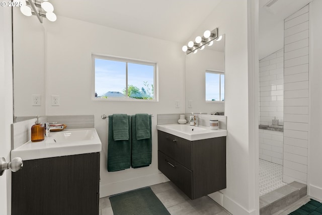bathroom featuring walk in shower, baseboards, two vanities, and a sink