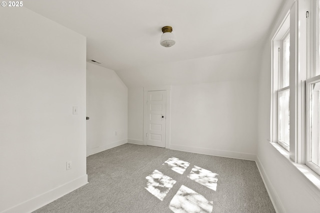 empty room with light colored carpet, vaulted ceiling, and baseboards