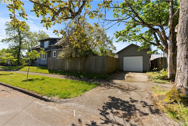 view of home's exterior with fence, driveway, a yard, a garage, and an outbuilding