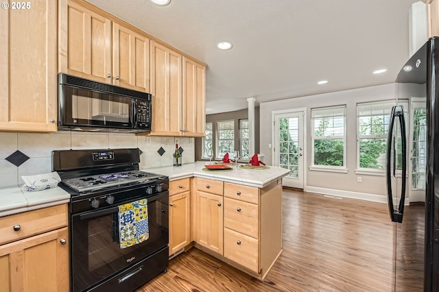 kitchen with black appliances, light brown cabinetry, a peninsula, light wood-style floors, and recessed lighting