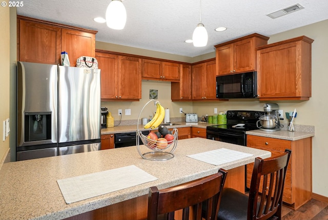 kitchen with a breakfast bar, a textured ceiling, sink, black appliances, and hanging light fixtures