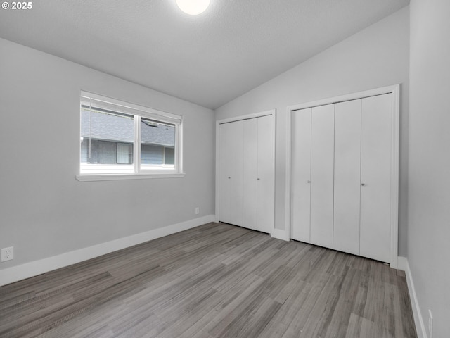 370 4th Pl, Manzanita, OR 97130 - unfurnished bedroom featuring multiple closets, vaulted ceiling, wood finished floors, baseboards, and a textured ceiling