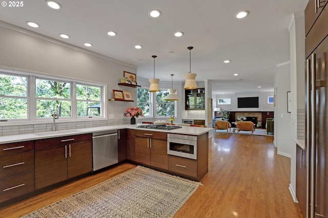 kitchen with backsplash, appliances with stainless steel finishes, a sink, light countertops, and a peninsula