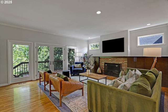 living room featuring a brick fireplace, recessed lighting, ornamental molding, and light wood-style flooring