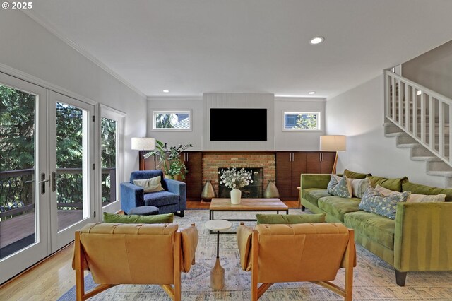 living area with french doors, crown molding, a fireplace, stairway, and light wood-style flooring