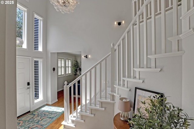 foyer entrance featuring an inviting chandelier, a towering ceiling, wood finished floors, and stairway