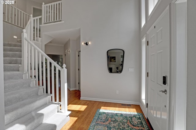 foyer featuring visible vents, wood finished floors, stairway, baseboards, and a high ceiling