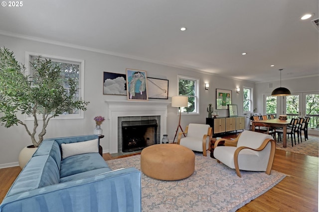living room with a tiled fireplace, recessed lighting, ornamental molding, and light wood finished floors