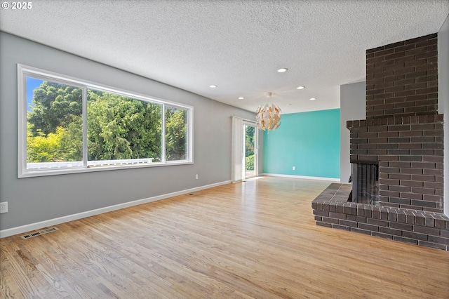 721 NW 76th St, Vancouver, WA 98665 - unfurnished living room with wood finished floors, a chandelier, a brick fireplace, baseboards, and a textured ceiling