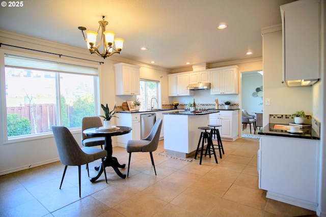 kitchen featuring light tile patterned flooring, under cabinet range hood, ornamental molding, a center island, and dark countertops