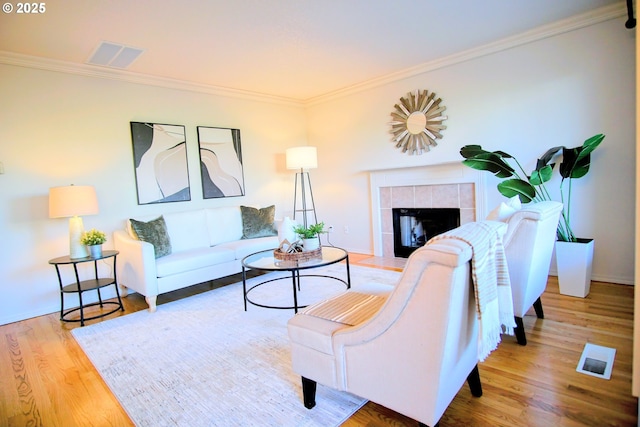 living area featuring visible vents, a fireplace, ornamental molding, and wood finished floors