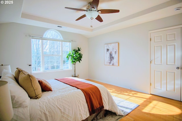 bedroom featuring visible vents, a tray ceiling, ceiling fan, and wood finished floors