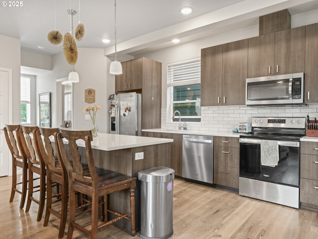 kitchen featuring appliances with stainless steel finishes, decorative light fixtures, tasteful backsplash, a breakfast bar area, and light wood-type flooring