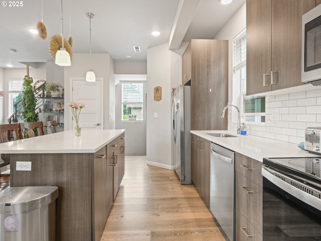 kitchen with sink, tasteful backsplash, decorative light fixtures, stainless steel appliances, and light hardwood / wood-style floors