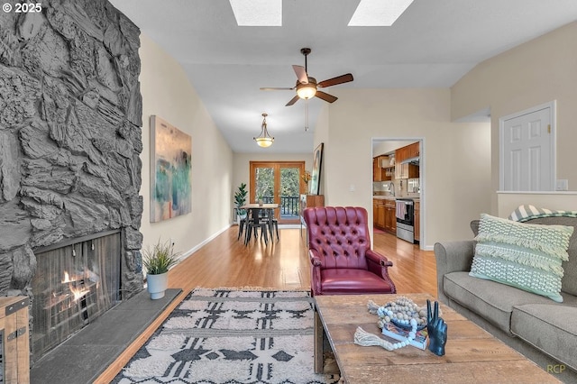 living area with light wood-style floors, vaulted ceiling with skylight, and a fireplace