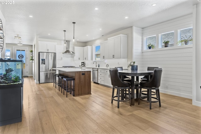 32750 Macy St, Eugene, OR 97408 - kitchen with appliances with stainless steel finishes, wall chimney exhaust hood, a kitchen bar, a center island, and light wood-style flooring