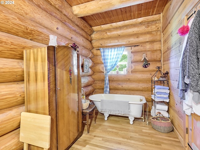 full bath featuring a freestanding tub, beam ceiling, wood finished floors, and log walls