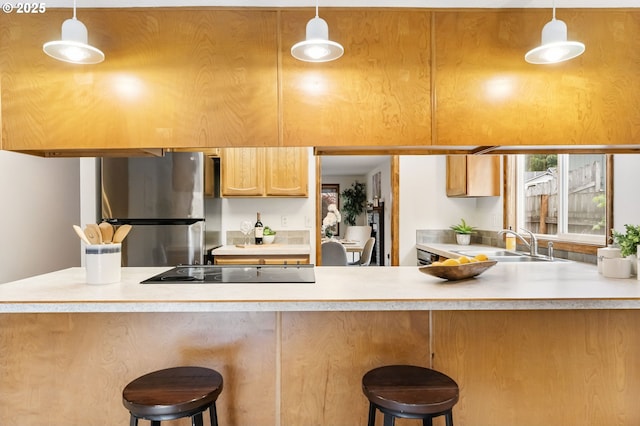 kitchen with freestanding refrigerator, a peninsula, black electric stovetop, light countertops, and a sink