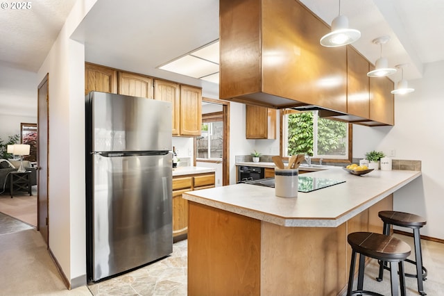 kitchen featuring black electric stovetop, a breakfast bar area, light countertops, freestanding refrigerator, and a peninsula