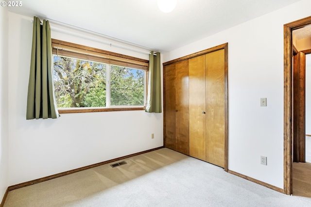 unfurnished bedroom featuring light colored carpet, baseboards, visible vents, and a closet