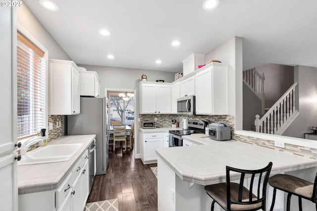 kitchen featuring kitchen peninsula, appliances with stainless steel finishes, white cabinetry, a breakfast bar, and tile counters